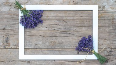 Menekşe demeti mor lavanta çiçekleri, otlar ve beyaz boş çerçeve, yazı için alanı olan kırsal ahşap masa dokusu manzarası.