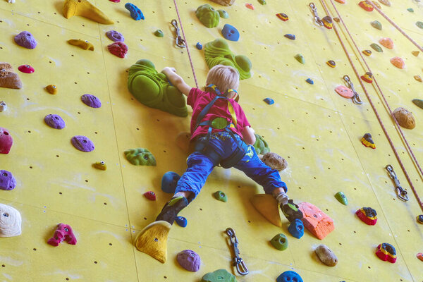 Маленький ребёнок (мальчик) лазает по боулдерингу в тренажерном зале