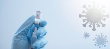 CORONAVIRUS COVID-19 / CORONA VACCINATION - Doktorun elinde şırınga ve Corona aşısı var, mavi arka planda virüs sembolü ile izole edilmiş.