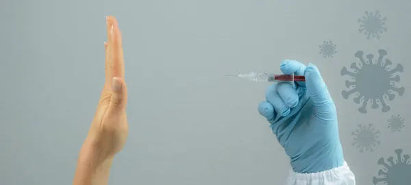 CORONAVIRUS COVID-19 / CORONA VACCINATION: NO FORCED VACCINATION, doctor holds syringe with Corona vaccination in his hand, hand of young woman refuses vaccination ( stop, no )