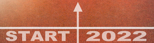 New year 2022 or start straight concept background banner panorama. Word START 2022 written on the orange running track on sports field with arrow, top view