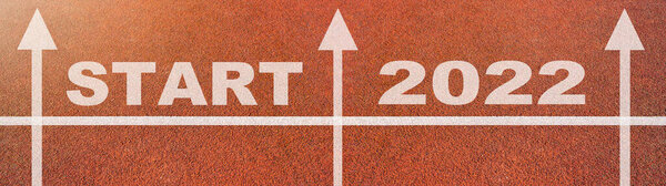 New year 2022 or start straight concept background banner panorama. Word START 2022 written on the orange running track on sports field with arrow, top view