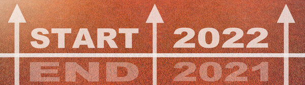 New year 2022 or start straight concept background banner panorama. Word START 2022, END 2021 written on the orange running track on sports field with arrow, top view