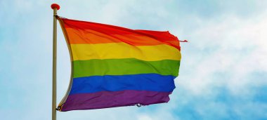 LGBT arkaplanı - Gökkuşağı bayrağı bulutlu mavi gökyüzünde dalgalanıyor
