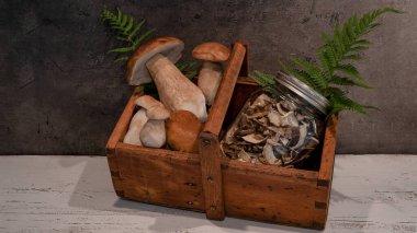 Gıda fotoğrafçılığı geçmişi - Taze ve kurumuş orman mantarları / Boletus edulis (kral bolete) / penny bun / cep / porcini / mantar, masadaki ahşap sepette depolama bardakları