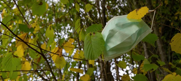 Coronavirus COVID-19 pandemic, new wave of infections in autumn - Antiviral medical protective mask,  for protection against corona virus. Surgical protective mask on autumnal tree with yellow leaves