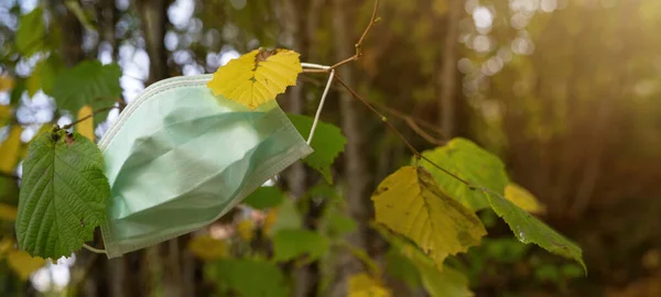 Coronavirus COVID-19 pandemic, new wave of infections in autumn - Antiviral medical protective mask,  for protection against corona virus. Surgical protective mask on autumnal tree with yellow leaves