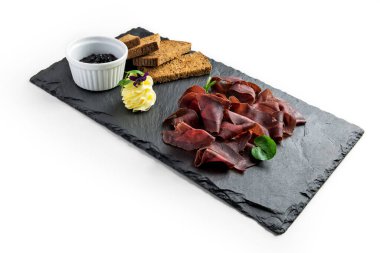 Beyaz arka planda siyah taş tabak, çavdar ekmeği reçeli ve tereyağı kreması.