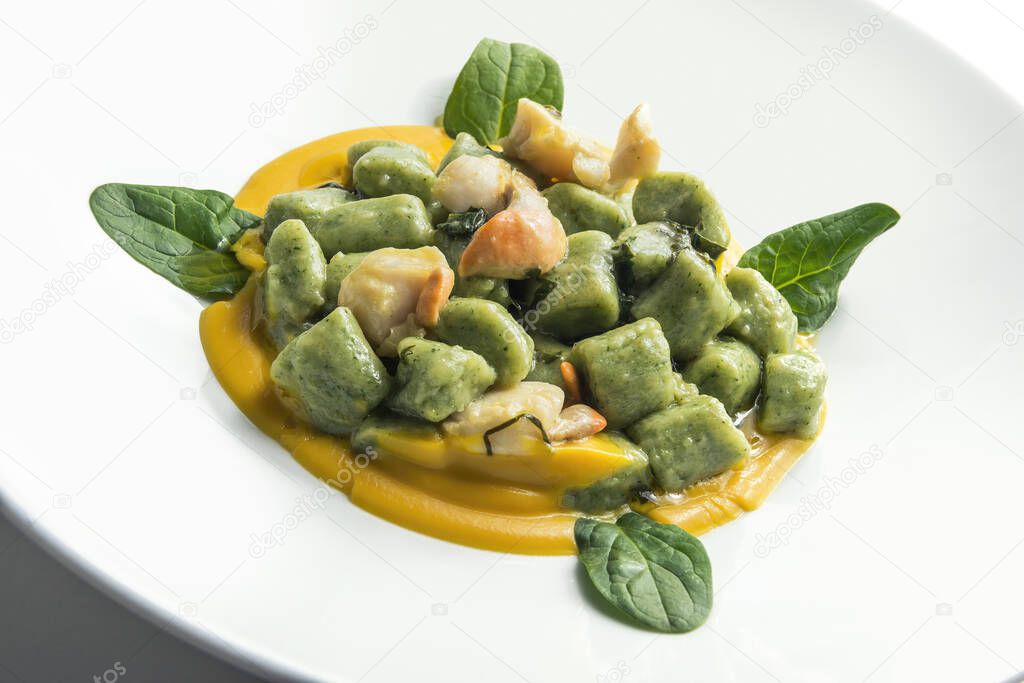 Plate of spinach gnocchi with pumpkin puree and scallops isolated on white background