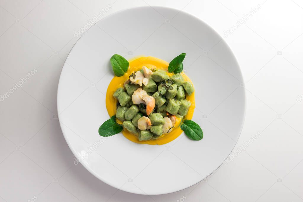 Plate of spinach gnocchi with pumpkin puree and scallops isolated on white background