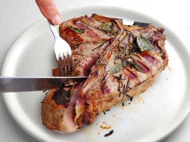 Beyaz arka planda yuvarlak beyaz bir tabakta kesilmiş ızgara Floransa bifteği.