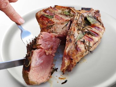 Beyaz arka planda yuvarlak beyaz bir tabakta kesilmiş ızgara Floransa bifteği.