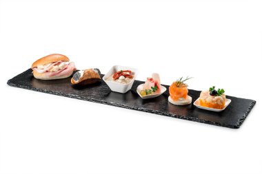Siyah taş dikdörtgen tepside karides tartar cannoli kılıçbalığı ravioli robiola tartina nordica mousse beyaz arka planda patlıcan
