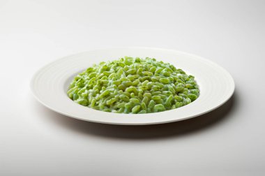 Beyaz arka planda yeşil sebzeli risotto ile beyaz yemek tabağı.