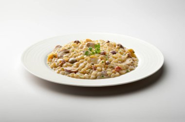 Beyaz arka planda maydanoz ve karışık mantarlı risotto tabağı.