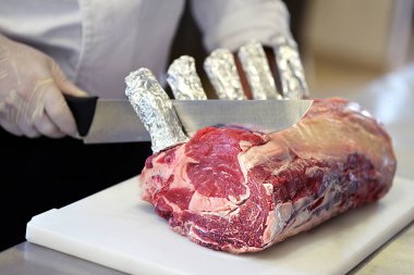 Kasap beyaz kesim tahtasındaki pirzolayı kesiyor.