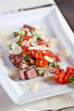 Kemikte pirzola, dikdörtgen bir tabakta domateslerle dilimlenmiş.