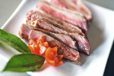 Kemikte pirzola, dikdörtgen bir tabakta domateslerle dilimlenmiş.