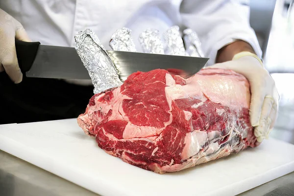 Detail of Butcher cuts rack of ribeye steak on white cutting board