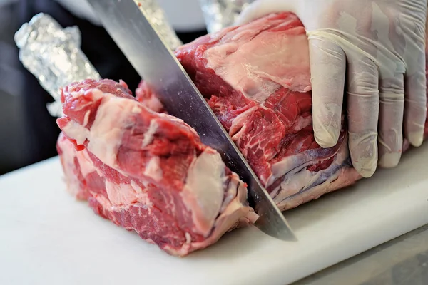 Detail of Butcher cuts rack of ribeye steak on white cutting board