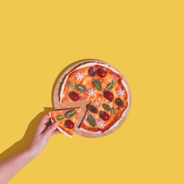 El, içinde Noel ağacı süsü olan bir dilim pizzayı malzeme olarak alıyor. Yeni yıl düz konsepti sarı arka plana karşıydı. Asgari yaratıcı fikir