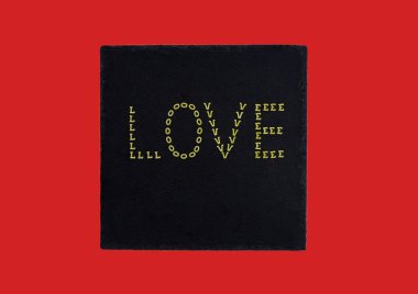 Kırmızı arkaplanda bir taş üzerine makarna ile yazılmış 'Aşk'.