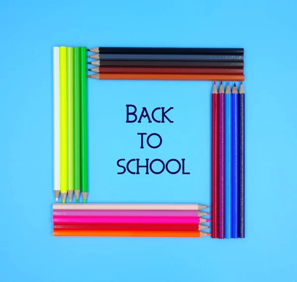 Crayons lie in the shape of a square. Colored pencils with text 'Back to school', isolated on a blue background.