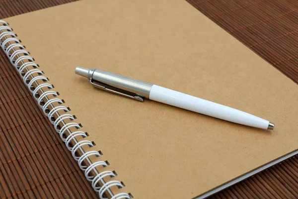 Recycled note book with white pen on a wooden background. Concept school and office supplies.