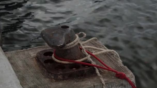 Een oude roestige mooring bolder met de touwen van vissersboten afgemeerd aan de steiger — Stockvideo