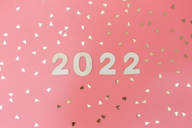 Pembe arka planda ahşap numaralar 2022 ve Noel ağacı şeklinde dağınık altın konfeti.