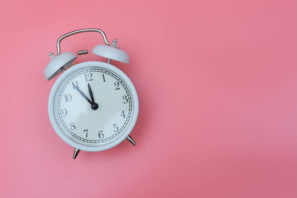 a white retro clock on a pink background shows 23.55