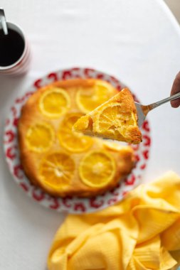 Omzunda portakallı turta parçası masanın üstünde, masanın üstünde bir fincan çay ve sarı bir havlu.