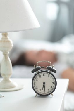 Çalar saat 6: 30 'da komodinin üzerinde, genç bir kadın parlak bir yatak odasında uyuyor.