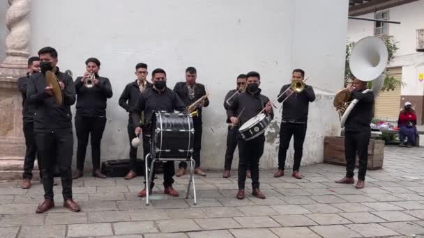 Cuenca, Ekvádor, 24. prosince 2021 - maskovaná kapela COVID hraje hudbu proti zdi kostela. — Stock video