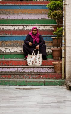 A woman sits alone on weathered colored stairs, holding her bag in Istanbul, Turkey