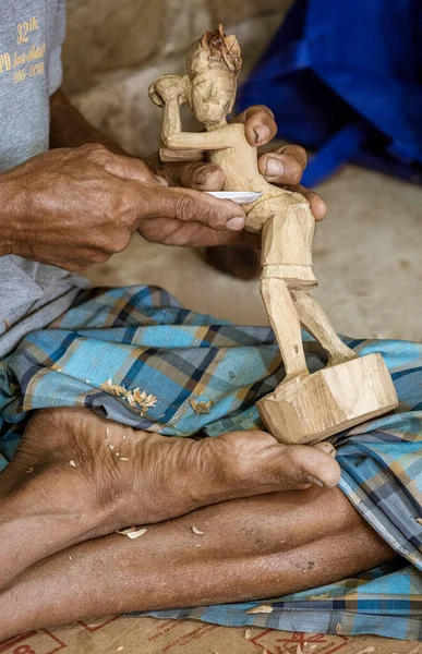 Man sits cross-legged while carving wooden statue.