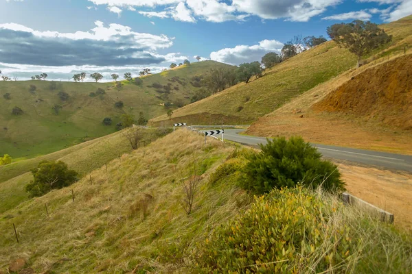 乾燥した芝生の丘の中腹の景色を通してオーストラリアの田舎道を巻き — ストック写真