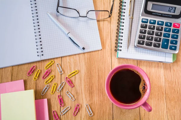 Bir fincan kahve, masaüstünde kalem, hesap makinesi ve bardak olan bir defter.