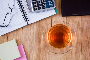 Bir fincan çay, masaüstünde kalem, hesap makinesi ve bardak olan bir defter. İş konsepti