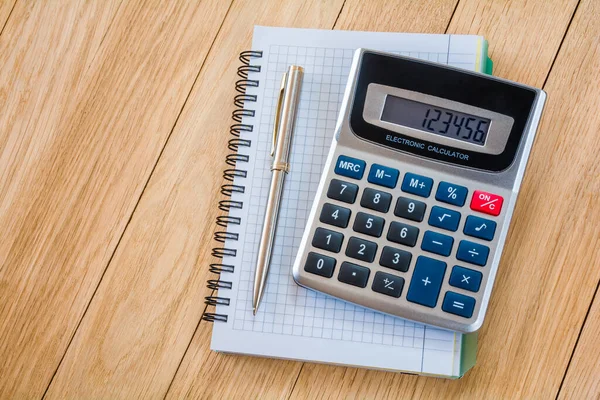 Tahta bir masa üzerinde kalem ve hesap makinesi.