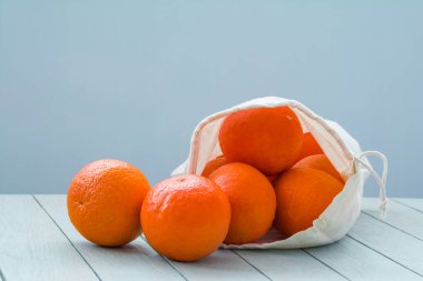 Fresh tangerines in a linen eco-bag on a light wooden table