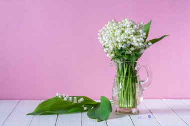 Pembe arka planda cam bir fincanda vadideki çiçeklerin güzel beyaz zambakları.