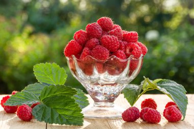 Bahçedeki ahşap bir masada şeffaf cam bir kasede taze ahududu.