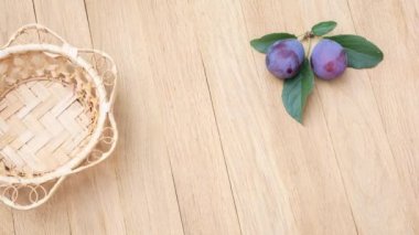 A wicker plate appears on a wooden table and is then filled with ripe plums. Stop motion animation