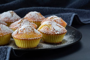 Taze pişmiş iştah açıcı kekler üzerine pudra şekeri serpiştirilmiş koyu yüzeyi olan siyah bir tabakta.
