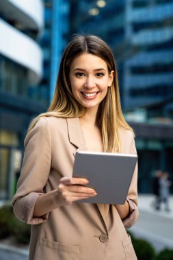 İş binasının önünde dikilirken dijital tablet kullanan başarılı çekici bir iş kadını. İş adamları konsept çalışır