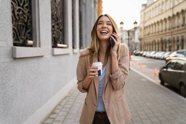 Çekici, genç ve başarılı bir kadın kahve içiyor ve molanın keyfini çıkarırken akıllı telefon kullanıyor.