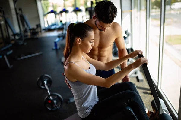 年轻男子私人教练帮助女人在健身房锻炼 健康生活方式体育人的概念 — 图库照片