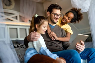 Evde dijital tabletle oynayan çok ırklı kızları olan mutlu bir baba.