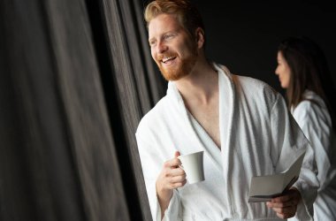 Genç, mutlu yakışıklı adam sabahları bornozlu kahve içiyor.